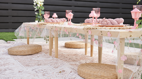 Styled picnic tables with blush place settings and woven floor cushions